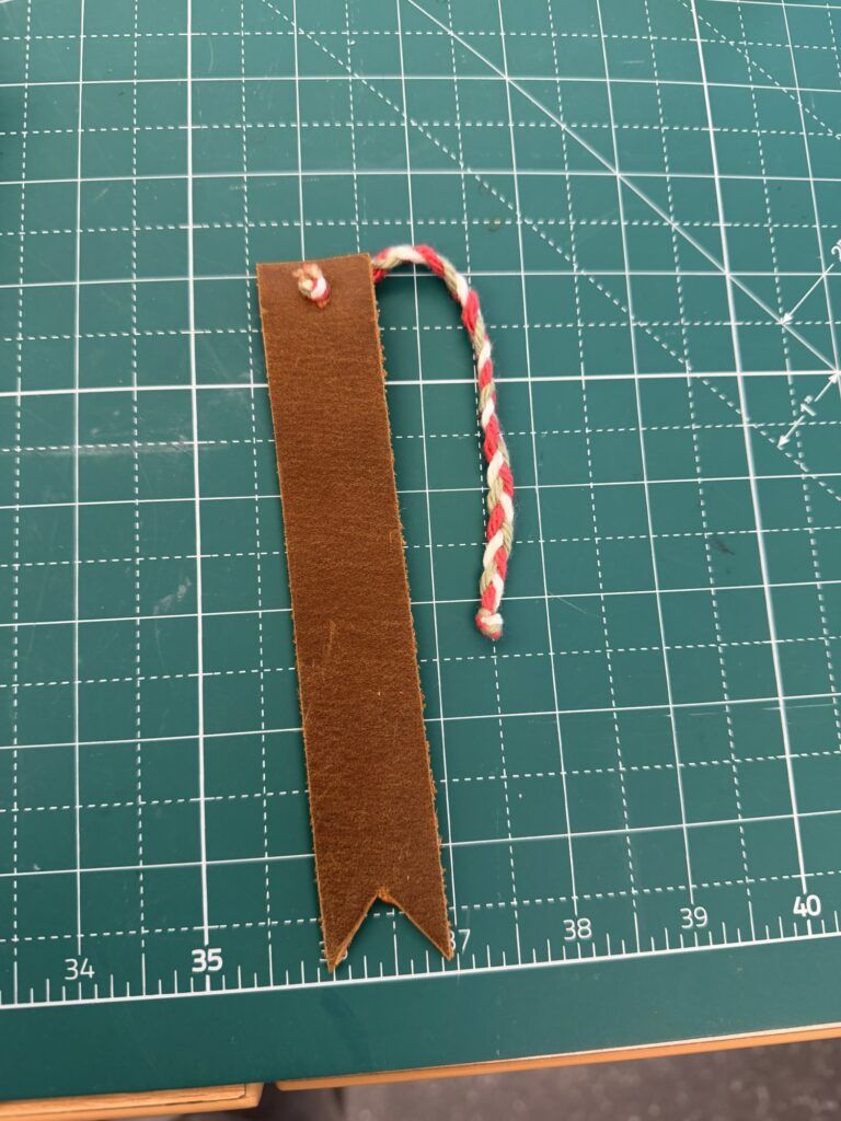 leather bookmark made from 1" wide leather, with a braided tassle of green, white, and red yarn.